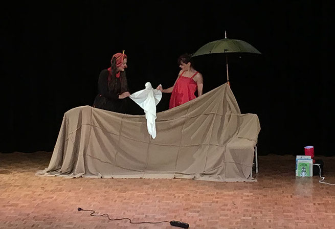 Le clown et la danseuse se tiennent derrière un drap tendu. Elles tiennent chacune un bras du chiffon.