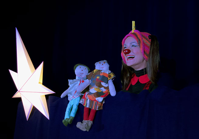 Le clown fait un grand sourire à côté de deux marionettes